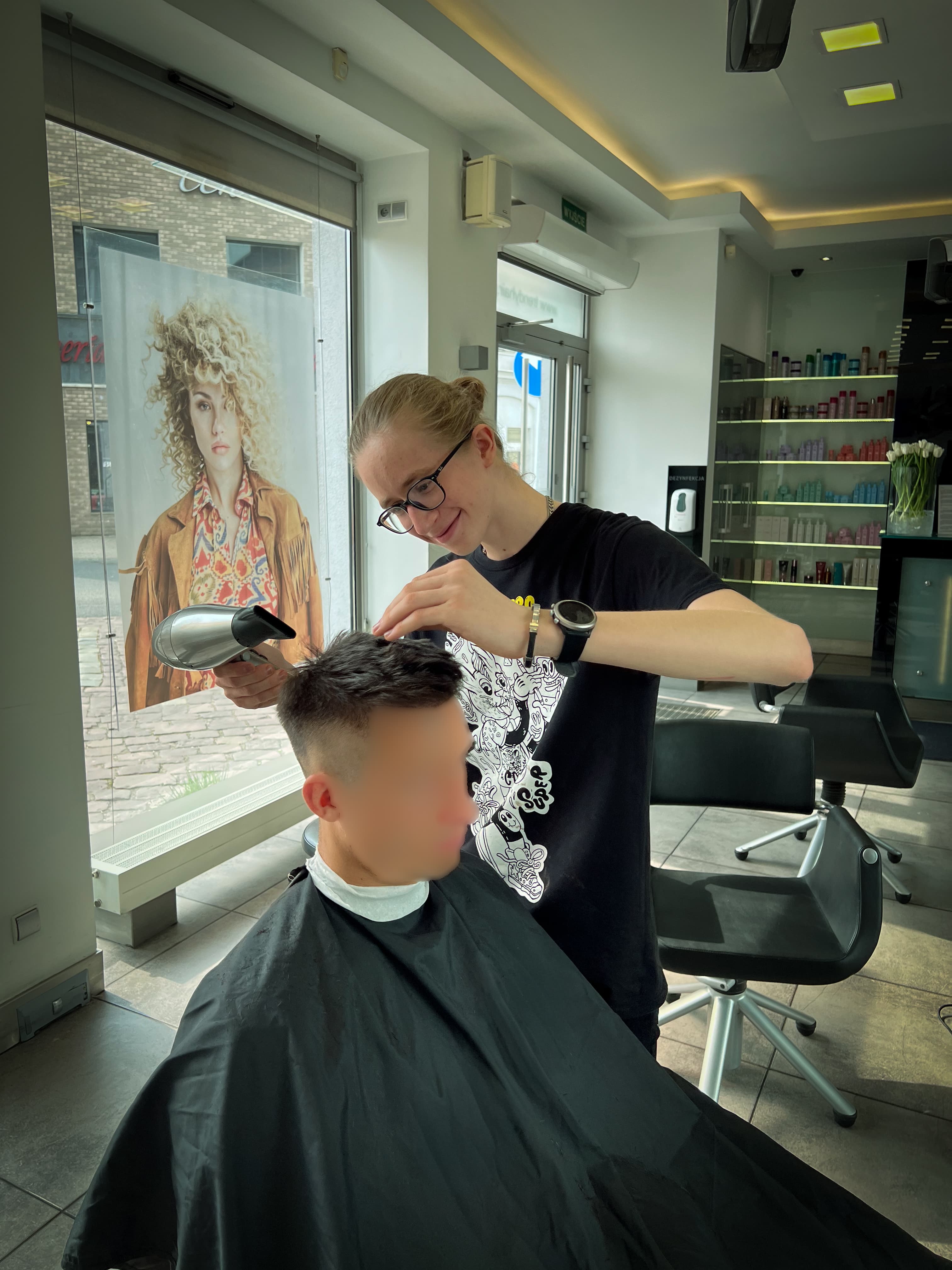Damian suszący włosy klienta suszarką w jasnym salonie fryzjerskim